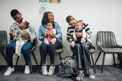 Group of parents sit with their babies in a waiting room
