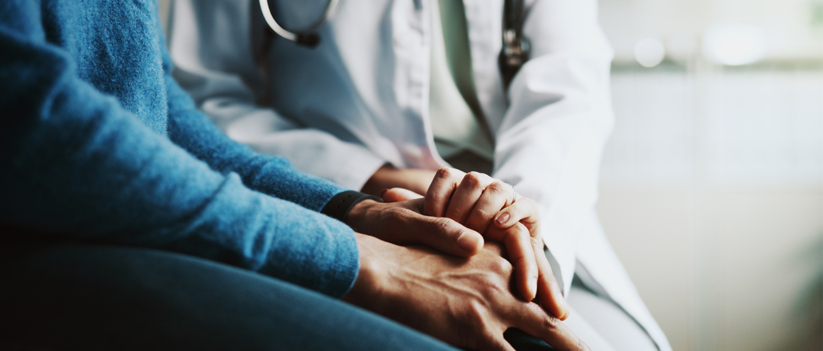 doctor in white coat and stethescope holds hands with patient in blue sweater