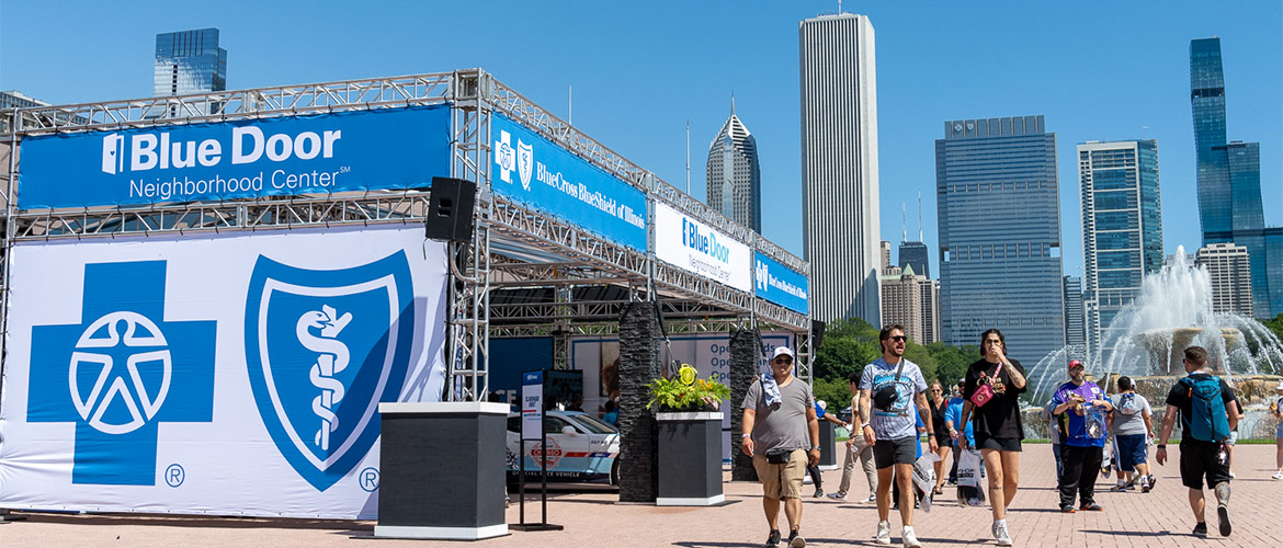 people walk outside near a pop-up health care site with skyscrapers in background