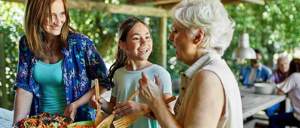 Two women and a girl talk as the girl mixes food in a bowl