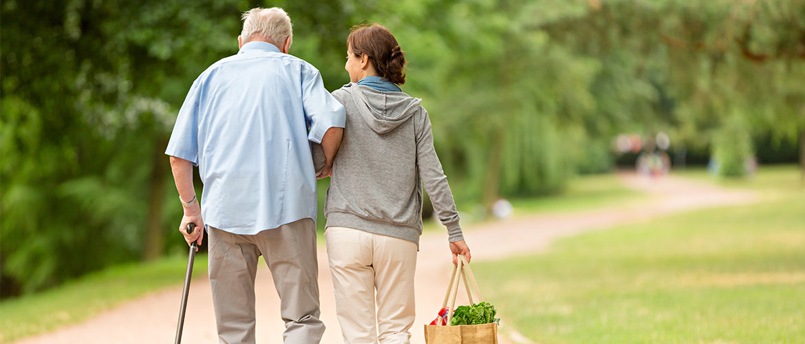 A woman assists an older man walking with a cane