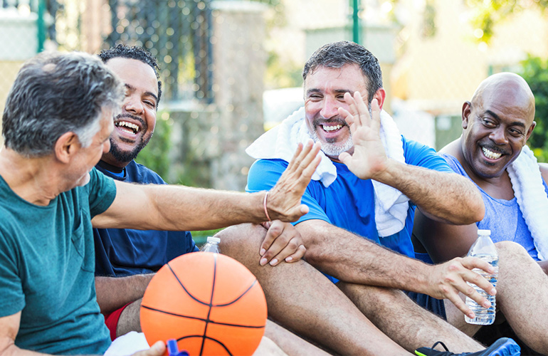 Two men sitting among a group of basketball players high-five each other