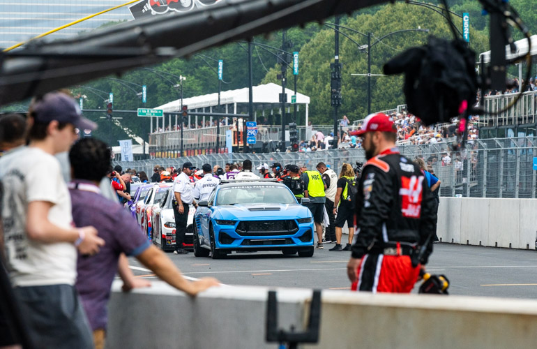 Racecars are in a single file line behind a blue pace car.