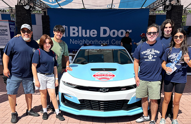 adults and teenagers stand outside near race car