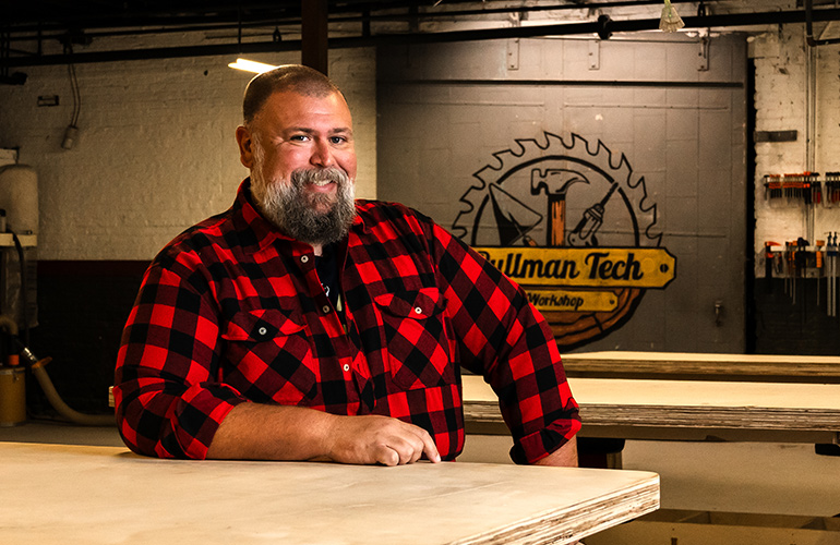 man with grey beard sits in woodworking workshop